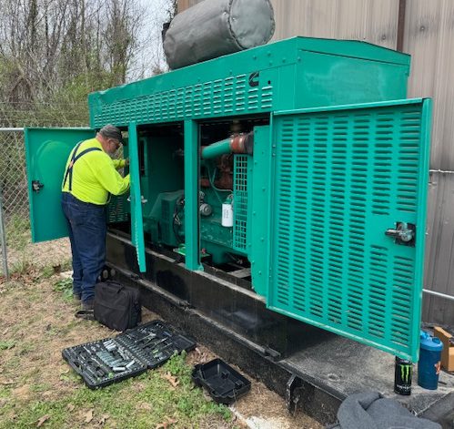 More about us at Benchmark Electric. Image of generator service technician performing routine generator maintenance on a Cummins diesel generator.